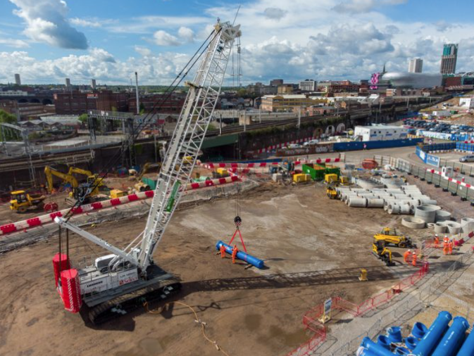 Large crane carrying blue pipe on bare construction site for HS2
